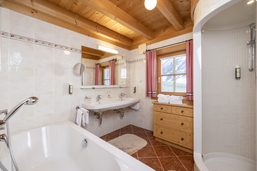 Helles Badezimmer im Erdgeschoss der Family Lodge Maximilian mit Dusche, Badewanne und Holzverkleidung.