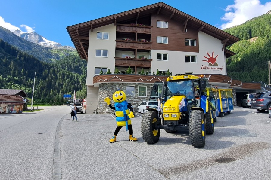 Maskottchen Kurt der Gletscherwurm steht vor dem Panoramazug und dem Hintertuxerhof.
