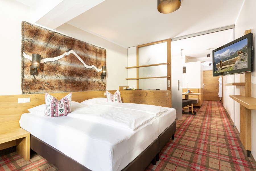 Schlafbereich der Juniorsuite Hintertux mit großem Doppelbett und Wand-TV.