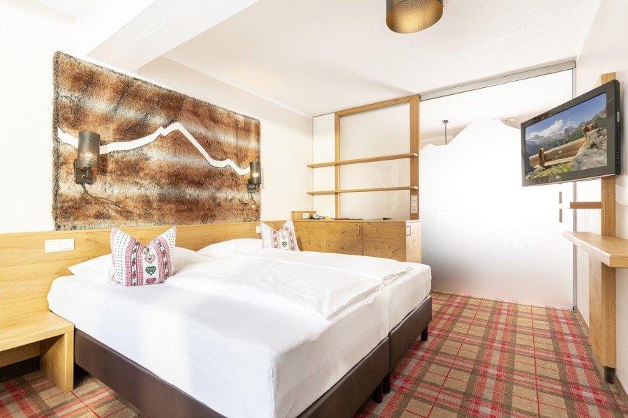 Gemütliches Schlafzimmer der Juniorsuite Hintertux mit geschlossener Schiebetür, alpinen Holzelementen und großen Fenstern.