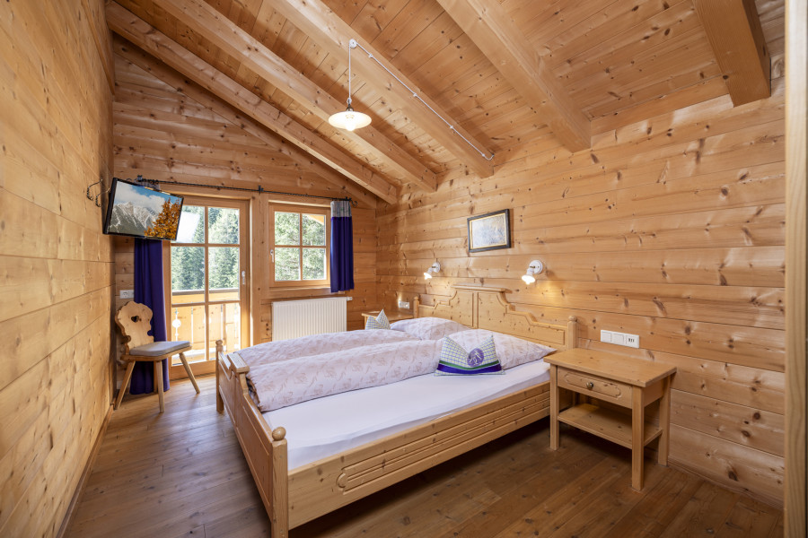 Schlafzimmer im Obergeschoss der Family Lodge Maximilian mit Holzdecke und Doppelbett.