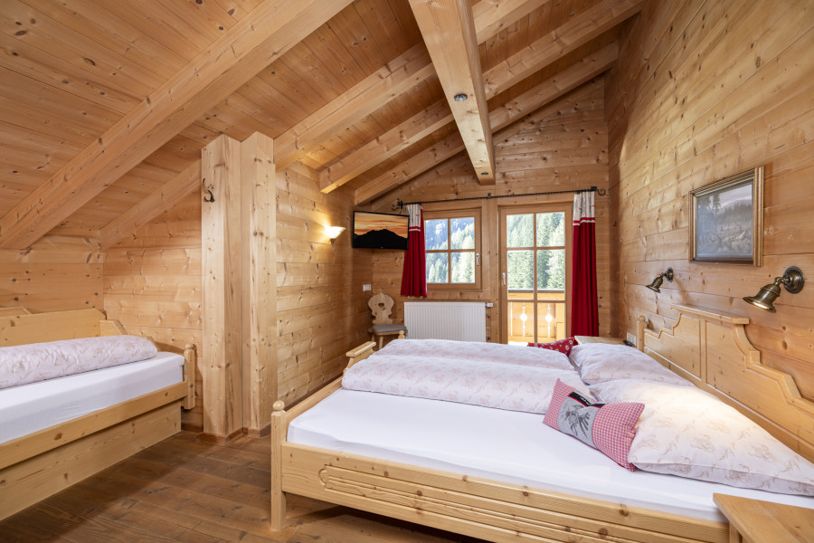 Schlafzimmer im Obergeschoss der Family Lodge Maximilian mit Holzdecke und Doppel- und Einzelbett.