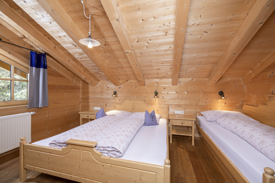 Schlafzimmer im Obergeschoss der Family Lodge Maximilian mit Holzdecke und Doppel- und Einzelbett.