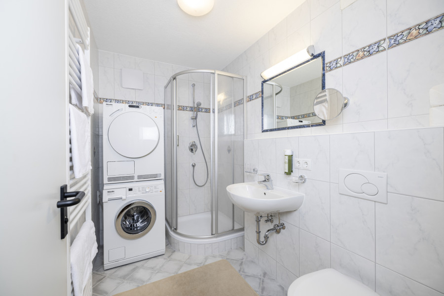 Badezimmer im Untergeschoss der Family Lodge Maximilian mit Dusche, Waschmaschine und Wäschetrockner.